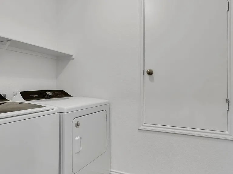 Dedicated laundry area with full-size washer and dryer, overhead shelving, and durable flooring for easy upkeep.