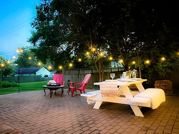 The brick and stone patio is equipped with a fire pit, string lights, a picnic table, and a grill