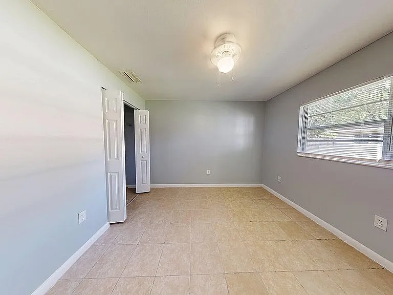 Bright and airy bedroom with neutral tones, large window for natural light, and modern tile flooring.