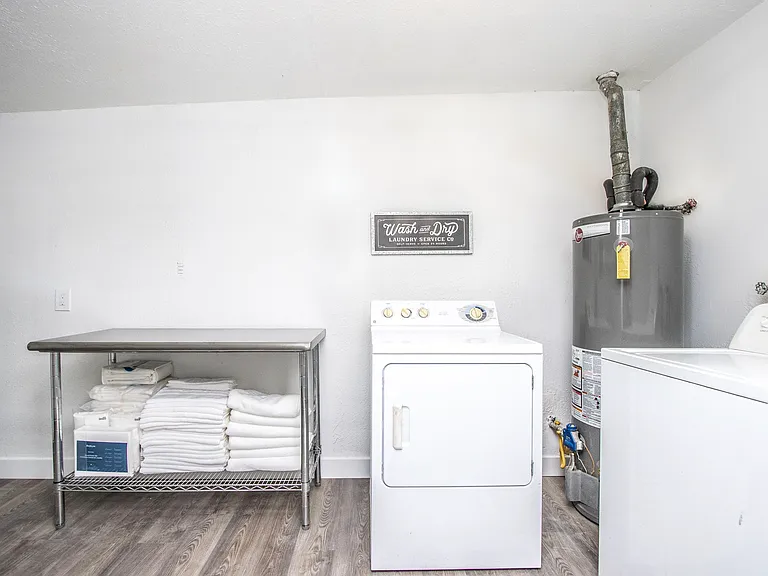 Convenient laundry room at Casa Del Sol, Tempe rental home. Features an in-unit washer and dryer, a stainless steel folding table with storage shelf, fresh linens, and a "Wash and Dry" sign. Practical amenity for a comfortable Tempe, AZ stay