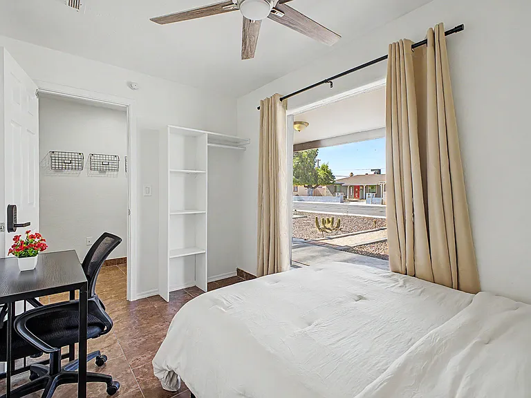 Private bedroom with a large window, ceiling fan, and tile floors, plus a dedicated desk area and open shelving storage.