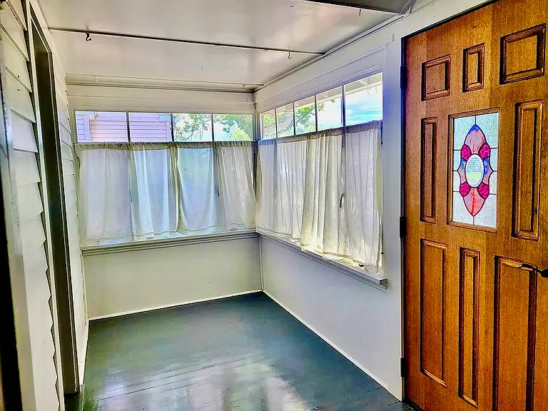 Front entry covered porch. Notice stained glass feature in original hardwood door. Painted wooden floor. Entry on left is to primary bedroom. Photo taken from entry to living area.
