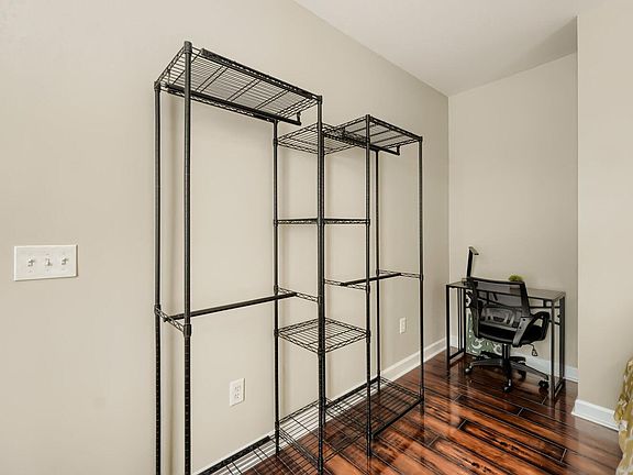 Bedroom corner with hardwood floors, open closet-style shelving, and a dedicated desk area for work or study.