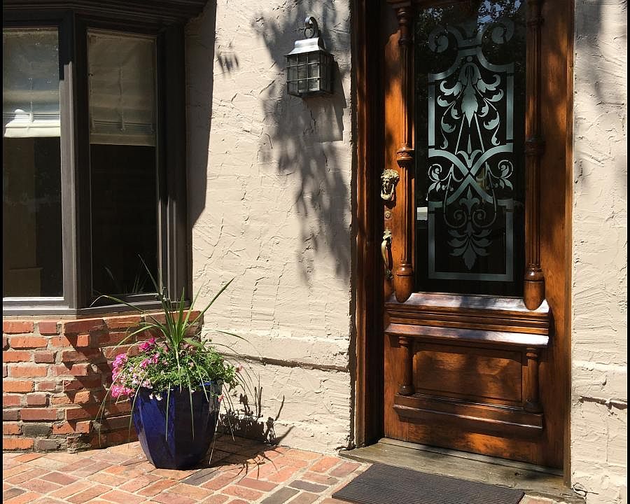Mahogany entry door with wrought iron coach light next to sunny window bay.
