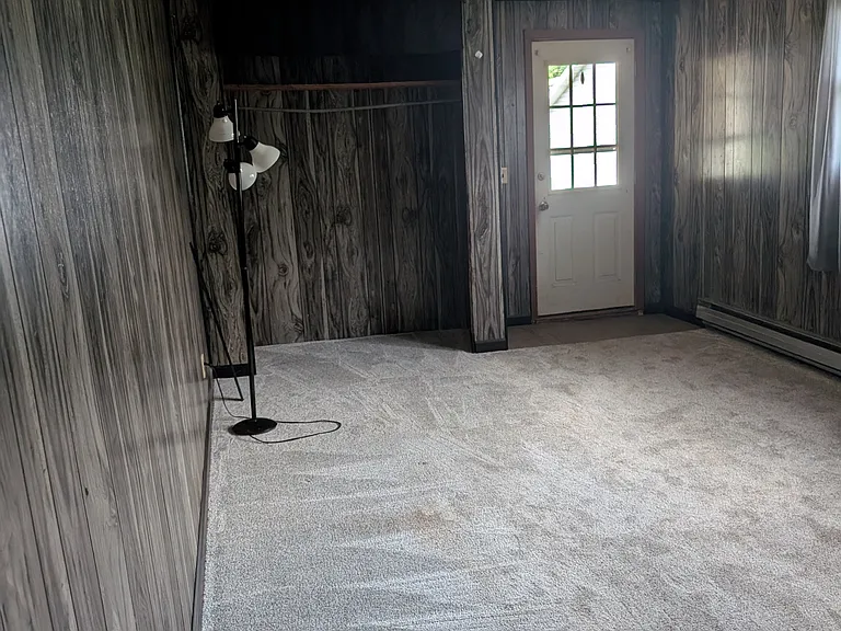 Large living room, entry door, closet by door, grey paneling, new grey carpet.