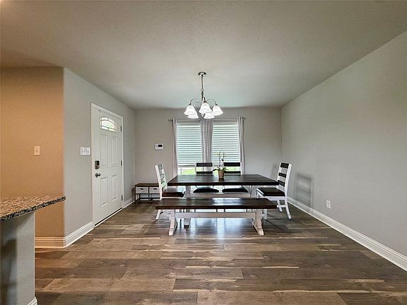 Open-concept dining area featuring wood-finish flooring, a contemporary chandelier, and a white paneled entry door with an arched glass insert