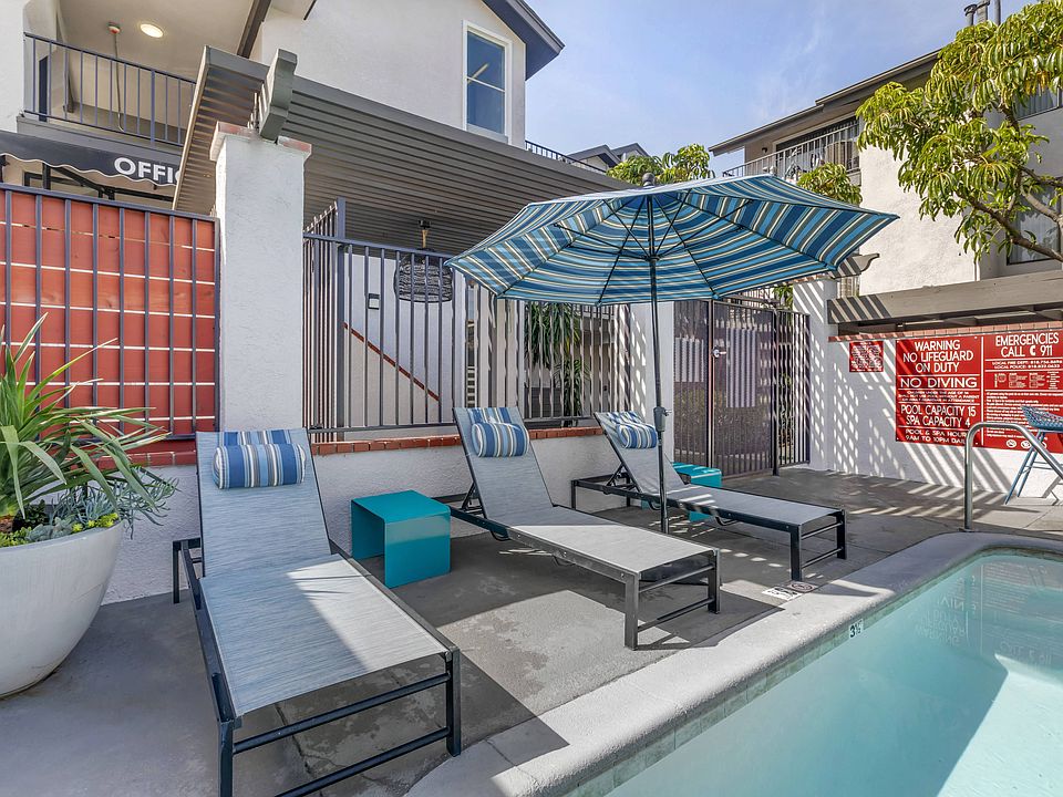 Relaxation meets luxury at Independence Plaza: Your oasis awaits, complete with a serene patio, sparkling pool, and inviting lounge chairs under the shade of a vibrant umbrella.