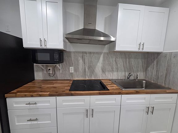 Modern kitchen featuring a stove, range hood, cabinets and essentials.