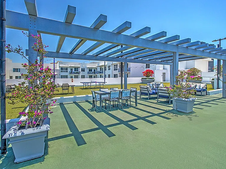 Luxury apartment rooftop lounge with pergola seating area, outdoor dining table, and city skyline views