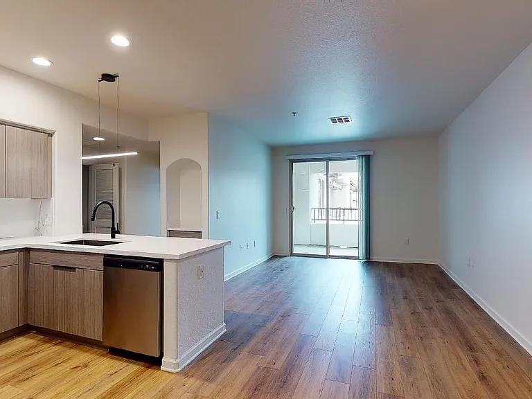 Apartment kitchen with stainless steel appliances, dining and living room with wood-style flooring.