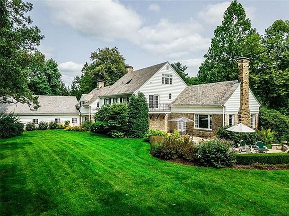 View of home from rear with large stone patios accessed from living areas & elegant privacy shrubbery leads out to the level law