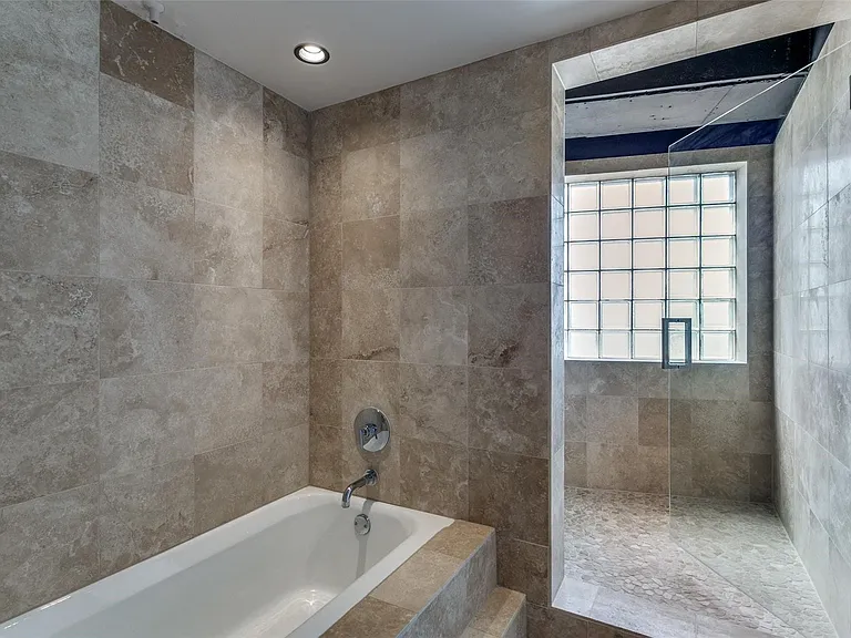 Tiled bathroom featuring a built-in tub and a separate glass-enclosed shower with a glass block window