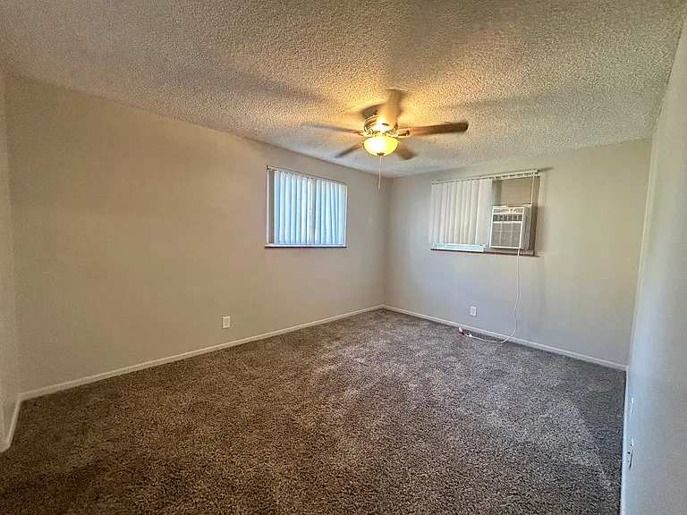 Spacious bedroom featuring plush carpeting, natural light from two windows, and a ceiling fan for comfort. Spacious bedroom featuring plush carpeting, natural light from two windows, and a ceiling fan for comfort.
