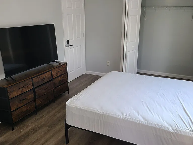 Furnished bedroom featuring a comfortable bed, dresser with TV, and a large closet for convenient storage.