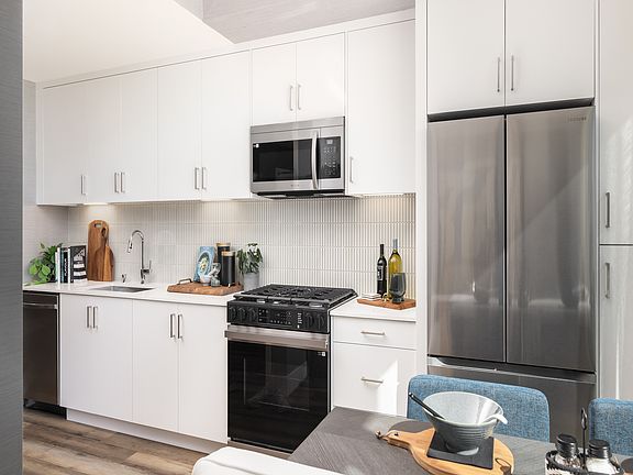 Bright, modern kitchen with sleek stainless steel appliances, abundant white cabinetry, and stylish wood flooring. Perfect for culinary creativity.