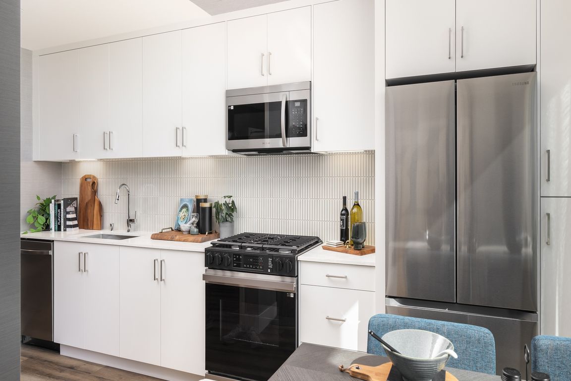 Bright, modern kitchen with sleek stainless steel appliances, abundant white cabinetry, and stylish wood flooring. Perfect for culinary creativity.