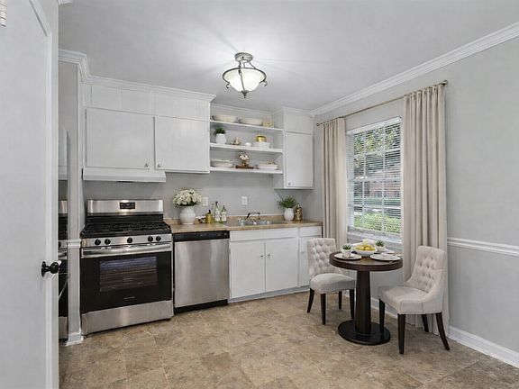 This sunlit, open kitchen offers crisp cabinetry, stainless appliances, warm floors, and a charming dining nook, creating a bright, inviting space that feels both comfortable and perfect for casual meals or entertaining.