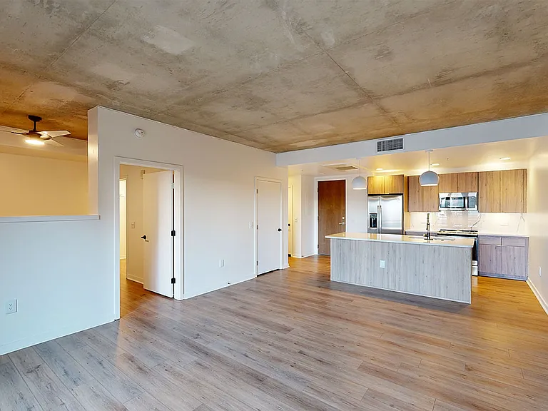 Apartment kitchen with stainless steel appliances, dining and living room with wood-style flooring.
