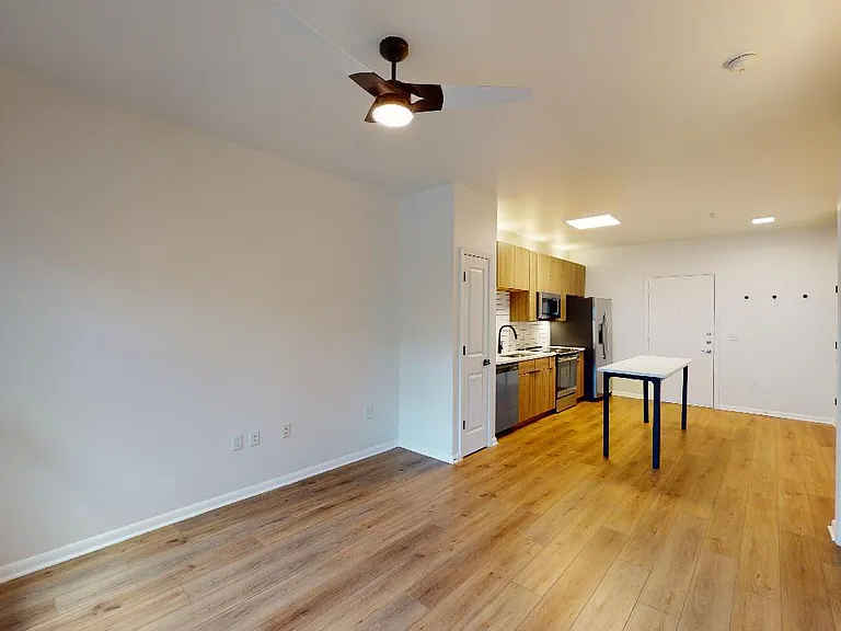 Apartment kitchen with stainless steel appliances, dining and living room with wood-style flooring.