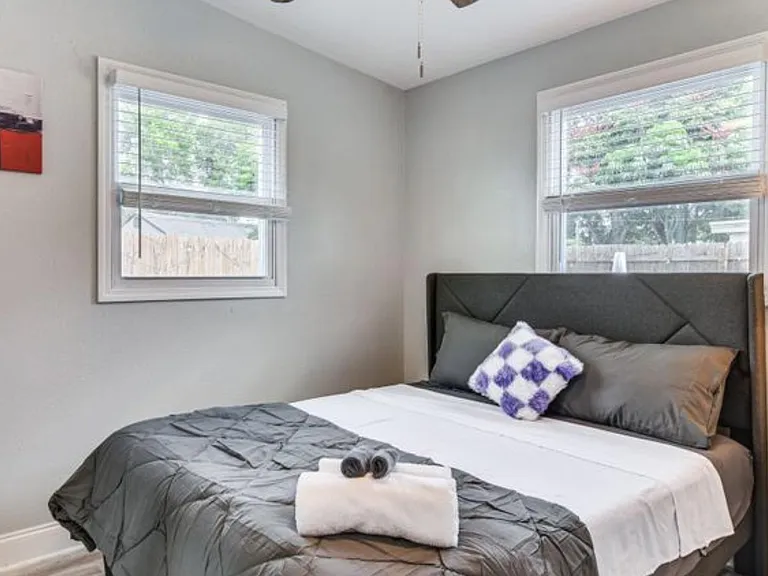 Furnished bedroom with a full bed, upholstered headboard, and two windows that provide natural light and backyard views.