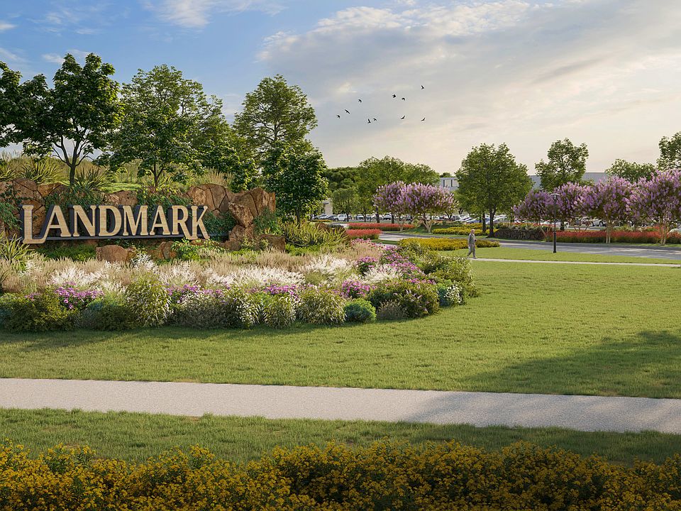 A lush, well-maintained park with a large Landmark sign in the foreground, surrounded by vibrant f