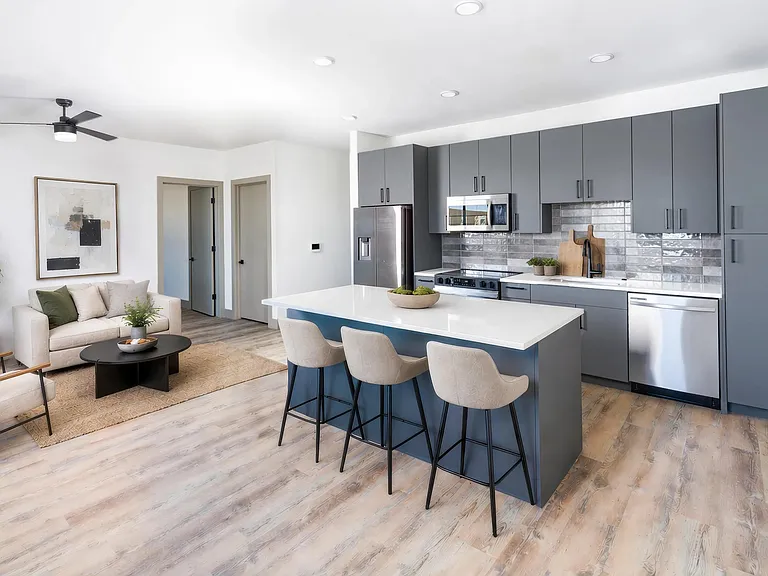 Open-concept kitchen and living area with a large island, stainless steel appliances, design-forward tile backsplash, and wood-style flooring throughout.
