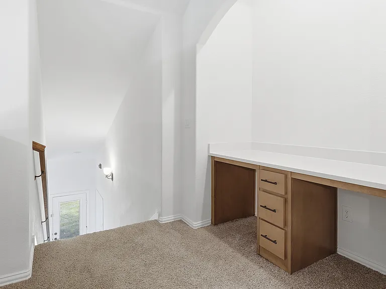 Built-in desk area featuring a light-toned countertop, wood-finish cabinetry with black hardware, and an arched alcove