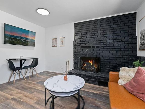 Living area with brick fireplace, seating and a small dining nook, finished with wood-look flooring and wall art.