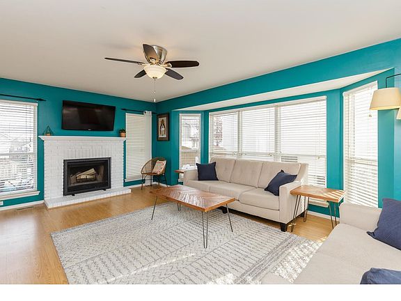 Large family room with expanded bay window, ceiling fan, laminate flooring, and wood burning fireplace.