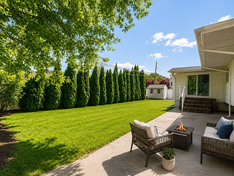 Fully fenced backyard surrounded by mature greenery, featuring a spacious patio and lawn area perfect for relaxing or entertaining