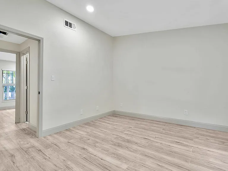 Bright and modern room with sleek wood flooring, fresh light walls, and ample natural light from a large window.