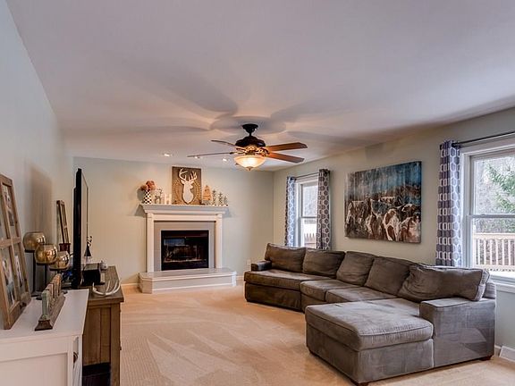 Family room in soft fresh neutral colors with natural light streaming through large windows. Focal point is wood burning fireplace, and ceiling fan circulates cool and warm air.