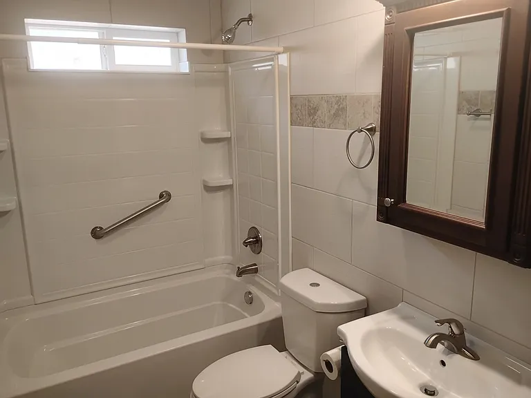 Sparkling clean bathroom has a full size bathtub with safety bar.