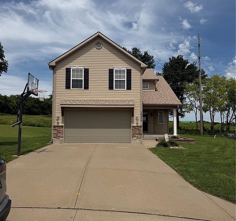 A concrete driveway leads to this two-story home featuring siding, shutters, and a garage.
