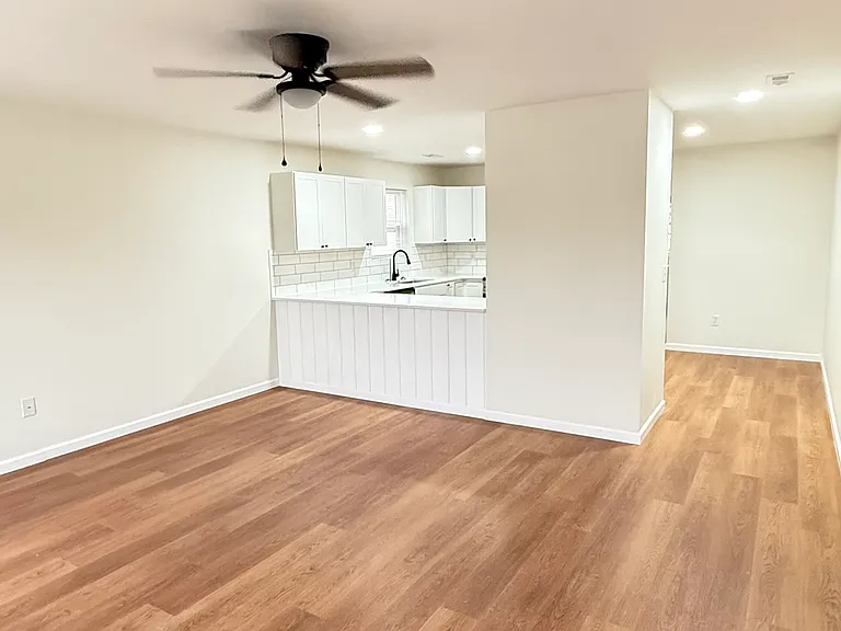 Living Room: Bright, spacious living room with a large window offering plenty of natural light, a ceiling fan, and an open-concept layout that flows seamlessly into the kitchen, creating a comfortable and inviting living space.