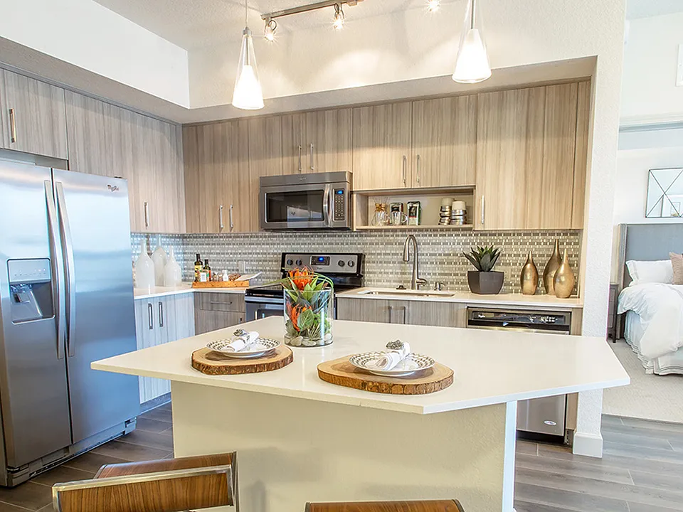 Open-concept luxury apartment kitchen with quartz island, stainless steel appliances, and wood cabinetry