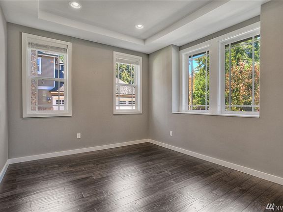 Light and bright formal living room features tray ceiling with recessed lights, arched doorway and engineered hardwood floors.