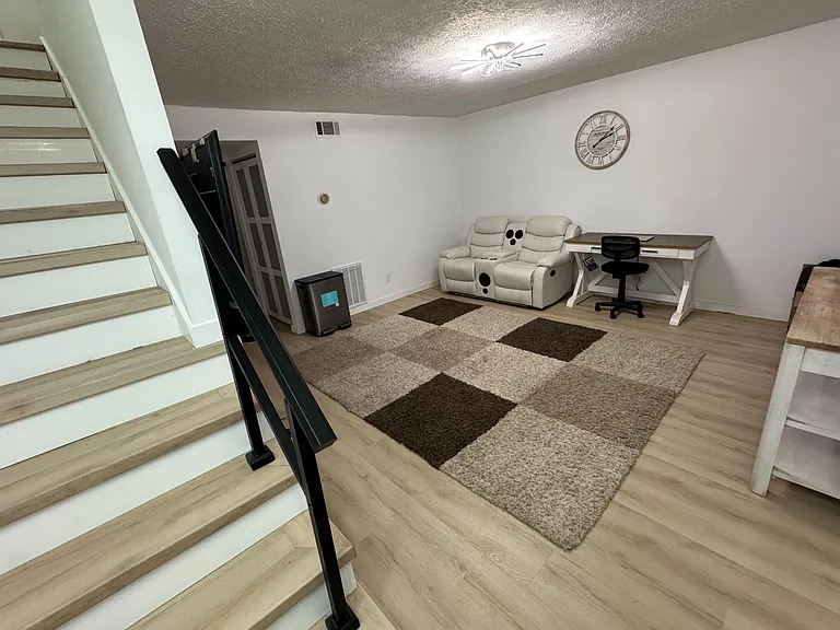 Lower-level lounge with reclining seating, a dedicated desk/work area, and durable wood-look flooring near the stairwell.