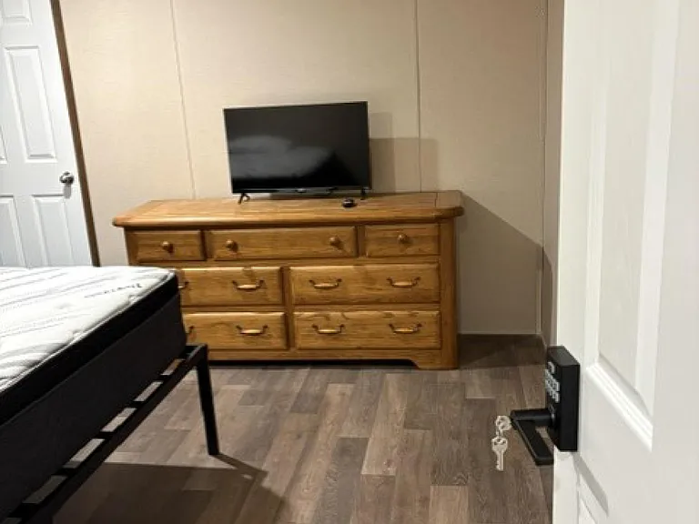 Furnished bedroom with wood-look flooring, a multi-drawer dresser, and a TV stand setup for easy relaxation.