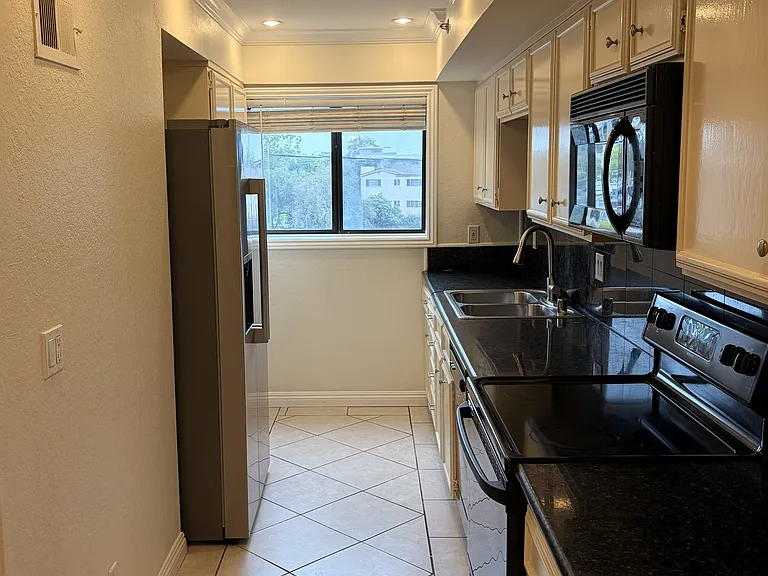 Bright galley kitchen with refrigerator, stove, microwave, dishwasher, and recessed lighting.