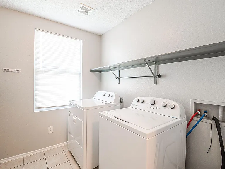 Dedicated laundry room with side-by-side washer and dryer, tiled flooring, and wall-mounted storage shelf.
