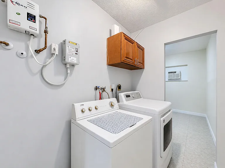 Dedicated laundry area with full-size washer and dryer, overhead storage cabinet, and easy-clean tile flooring.