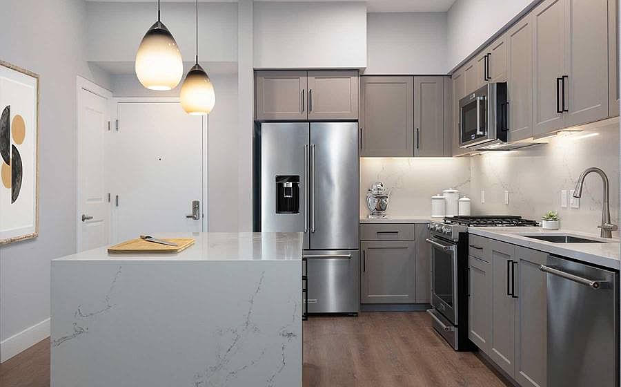 Phase II Signature Collection Kitchen with grey cabinetry, white marble countertops and backsplash, upgraded stainless steel appliances, and hard surface flooring