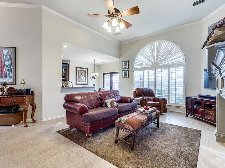 Large living room with fireplace. Tile floor and large windows with lots of natural light. Crown molding and ceiling fan.