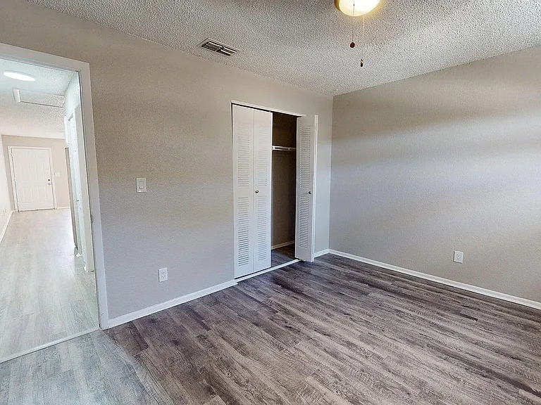 Bright and airy bedroom with stylish wood flooring and ample closet space, leading to an inviting hallway.
