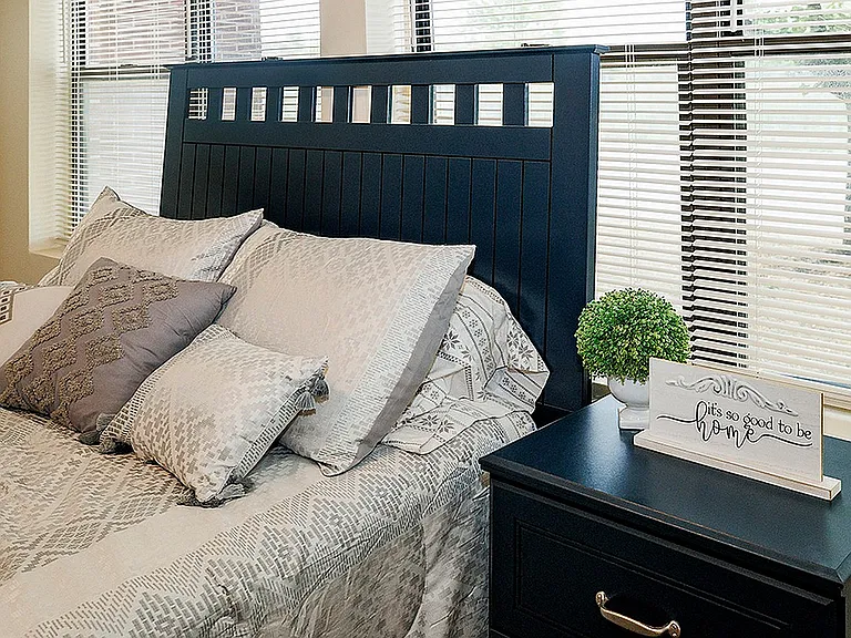 Cozy bedroom with elegant bedding, stylish dark wood headboard, and decorative accents, well-lit with natural sunlight.
