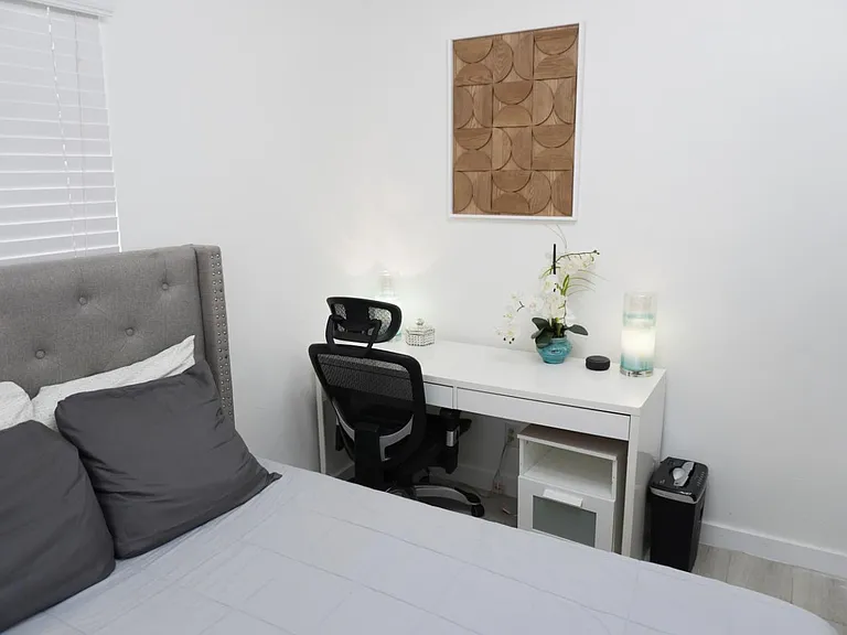 Bedroom features a comfortable bed, dedicated desk workspace, and window with blinds for privacy and light control.