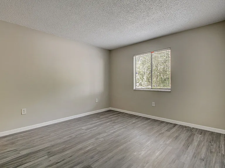 Bright, spacious bedroom with modern laminate flooring and a large window providing abundant natural light.