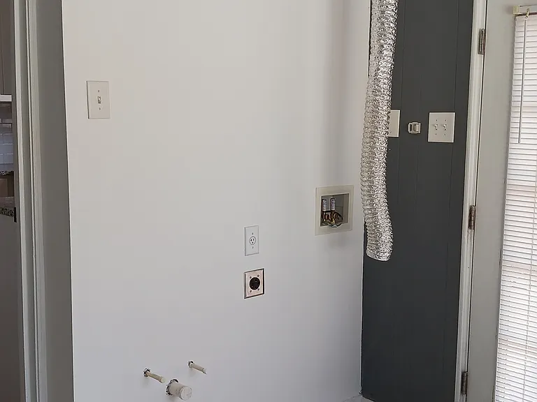 Newly finished wall in bonus room with washer/dryer hookups and plumbing for a utility sink.