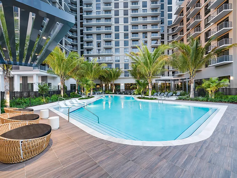 Resort-style pool design with curved entry steps, wood-look decking, and layered palms_ the epitome of Miami living.